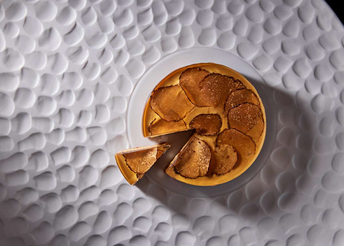 Truffle-topped tart slice served on a textured white plate in an upscale restaurant