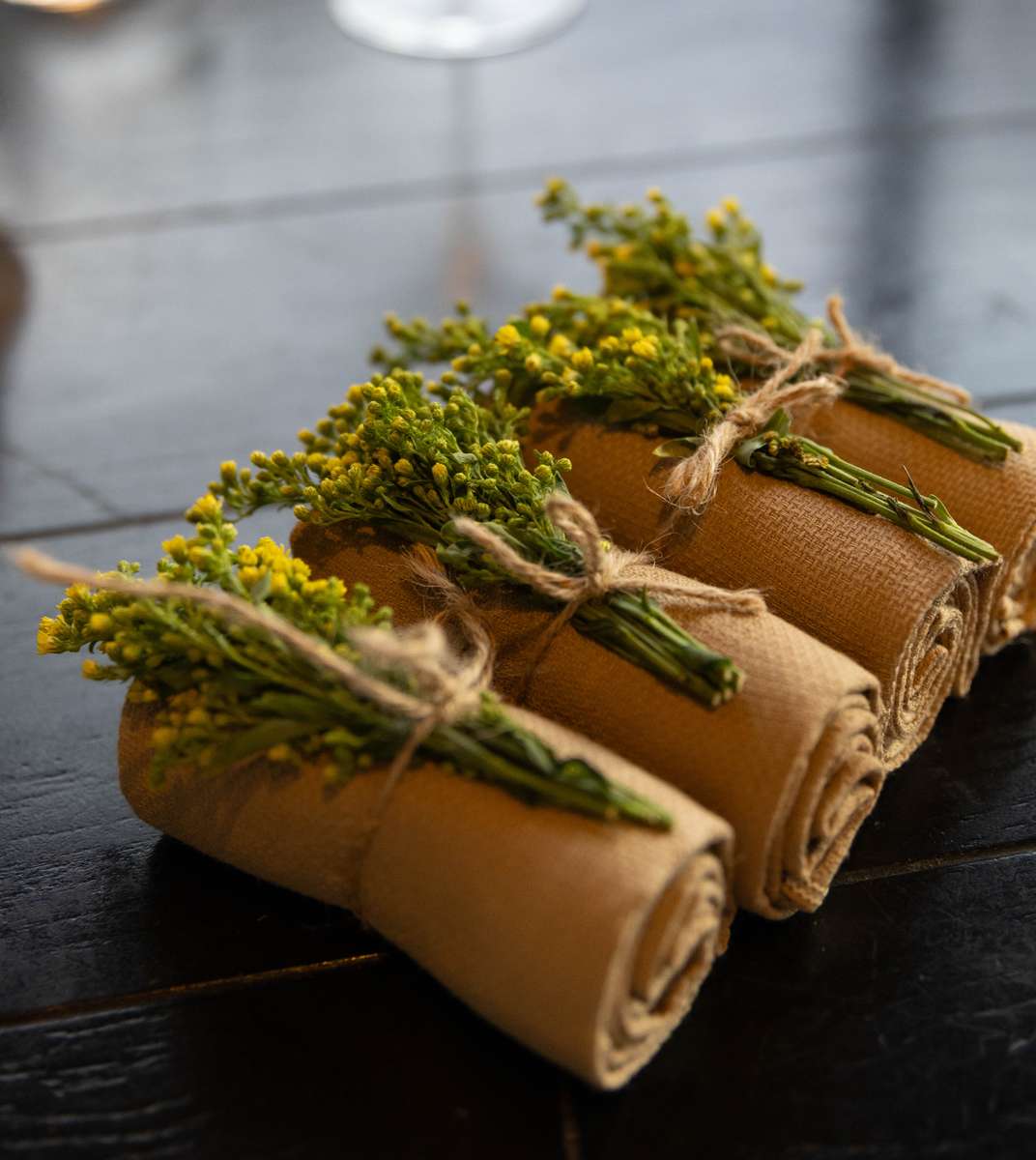 Rustic fine dining table setting with rolled linen napkins tied with twine and decorated with yellow flowers.