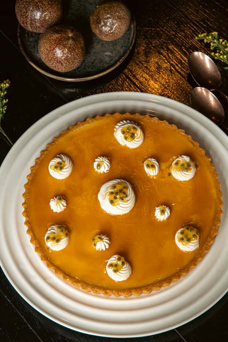 Passion fruit tart topped with whipped cream and fresh passion fruit seeds on a white plate