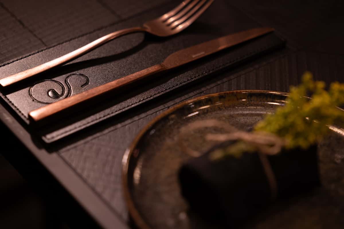 Elegant restaurant table setting with copper cutlery, black napkin, and moody lighting