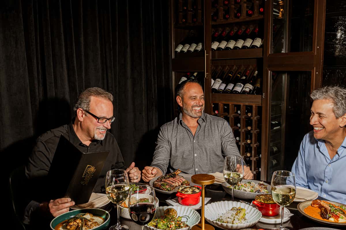 Three men enjoying a fine dining meal in Las Vegas, illustrating smart-casual restaurant attire for a guide on wearing jeans to fine dining.