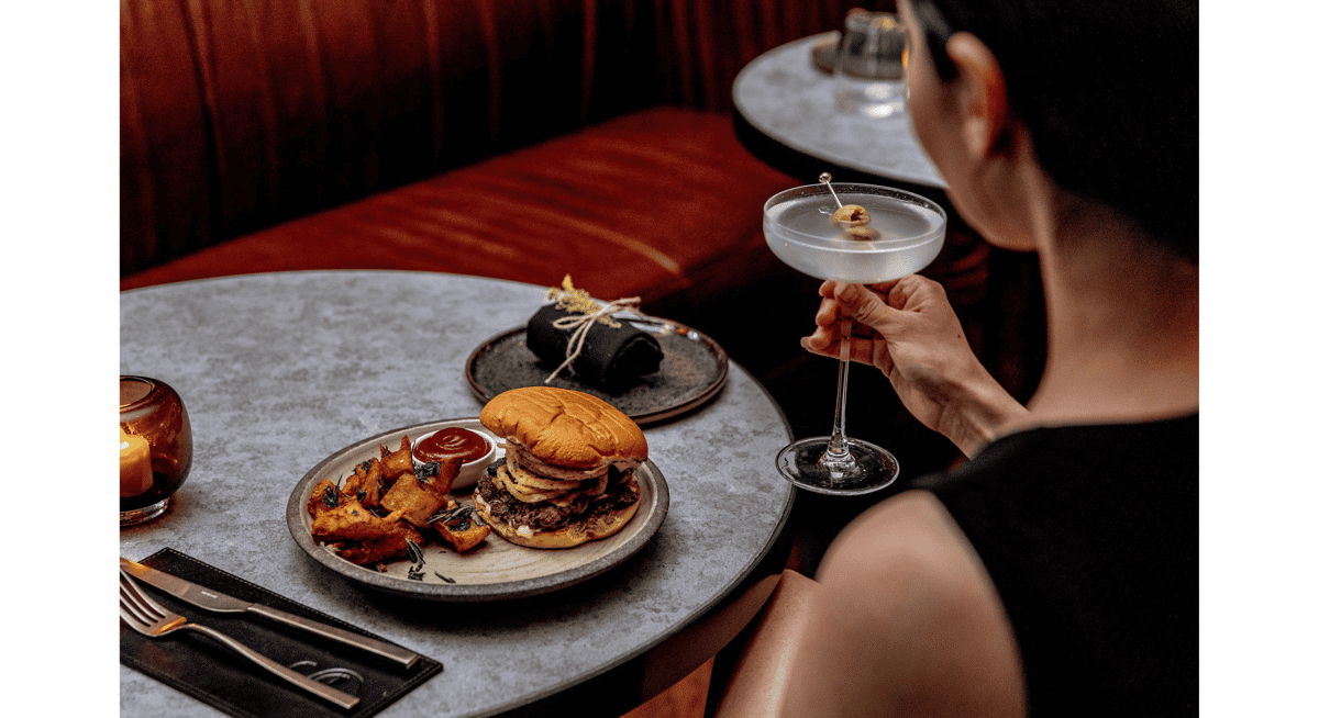 Gourmet burger with crispy potatoes served at upscale restaurant table with martini cocktail