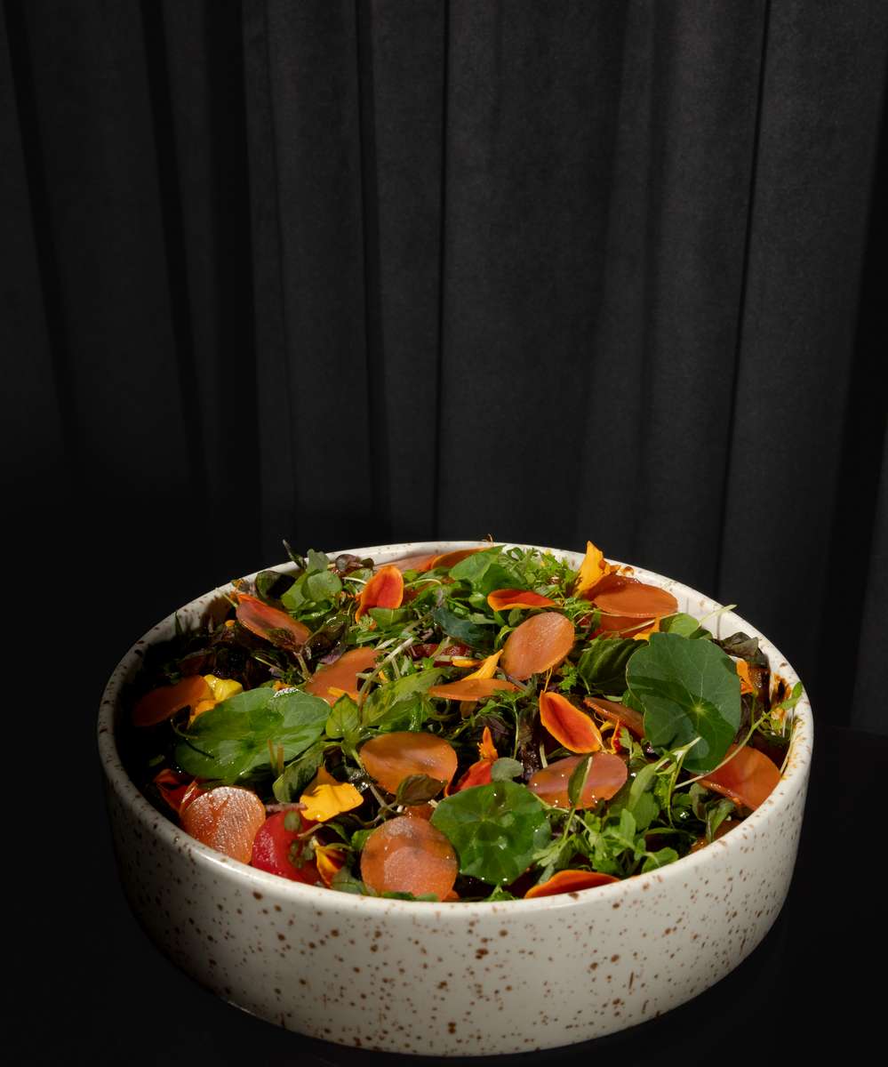 Colorful fresh herb salad with edible flowers and pickled vegetables in a speckled ceramic bowl.