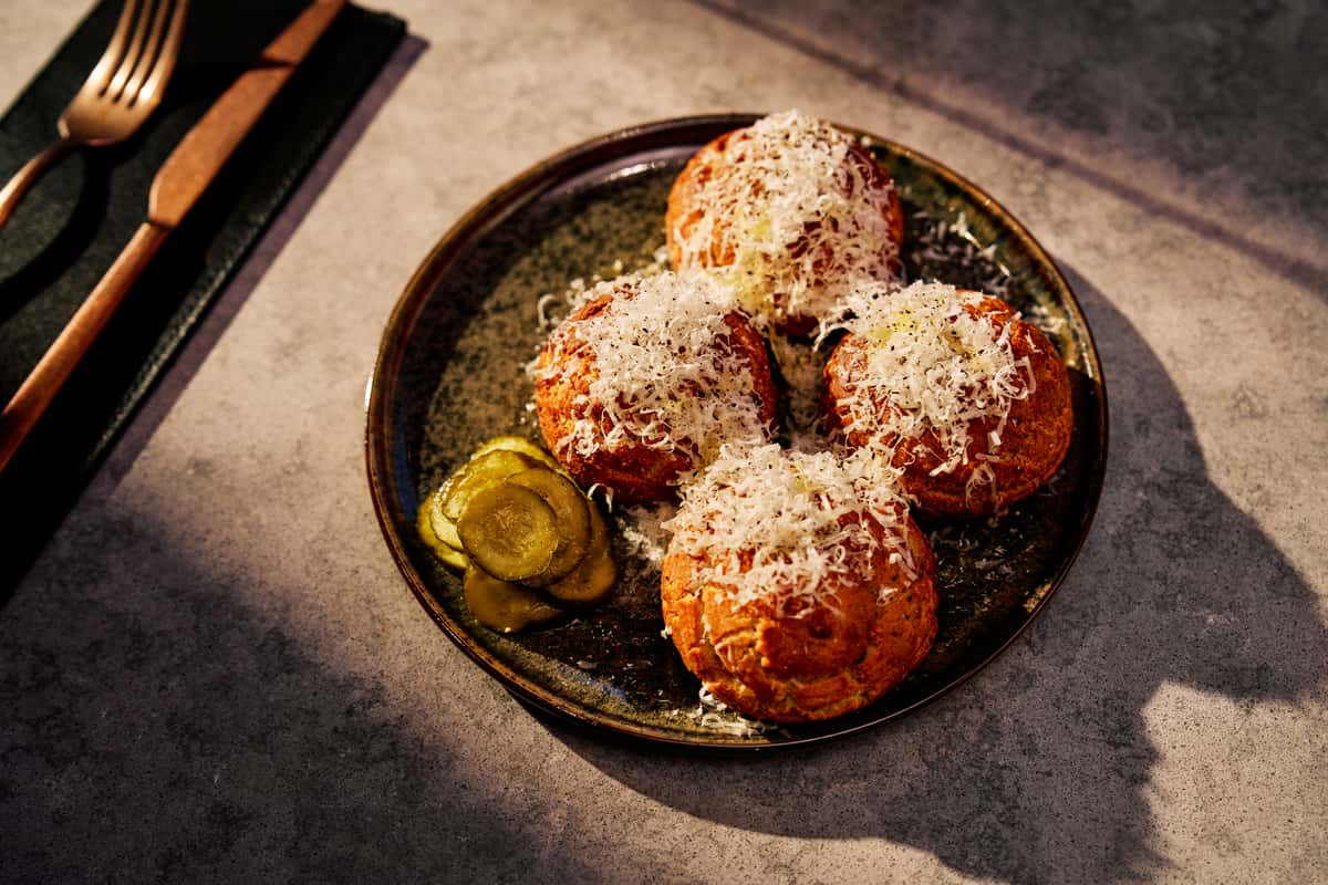 Savory cheese-topped bites served with pickles, highlighting accompaniments commonly paired with summer sausage.