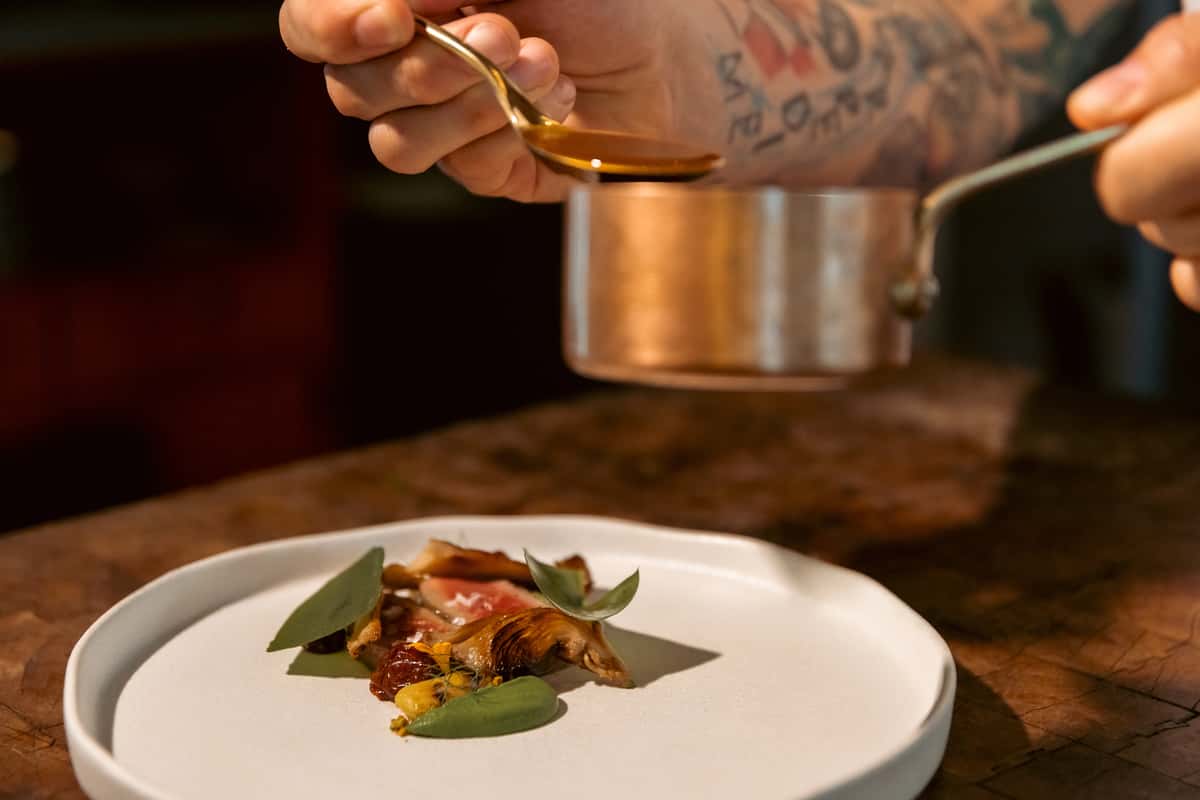 Chef spooning sauce over a plated fine dining dish