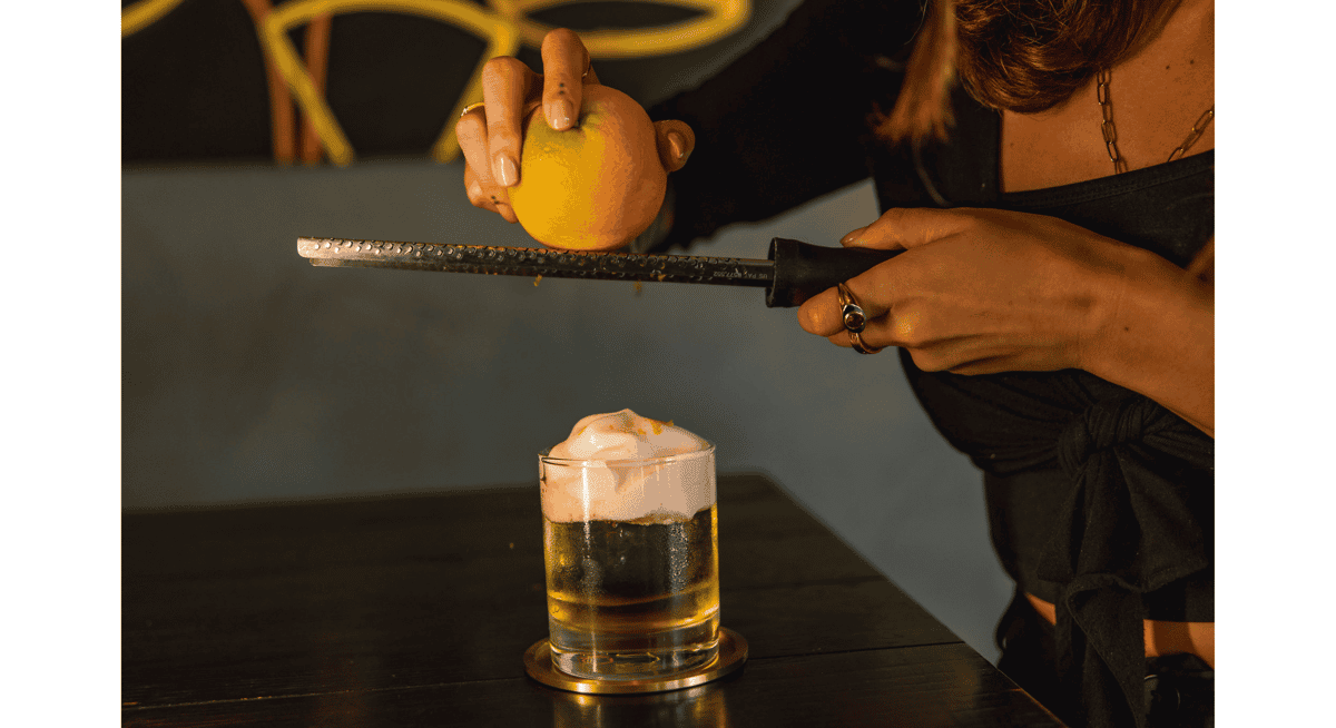 Bartender finishing a craft cocktail with fresh orange zest at Stubborn Seed Miami, highlighting an affordable way to experience Michelin-level dining.