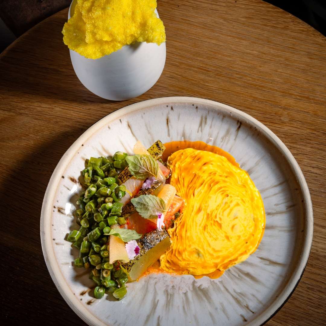 Fine dining plated dish with salmon, green beans, herbs, and yellow puree