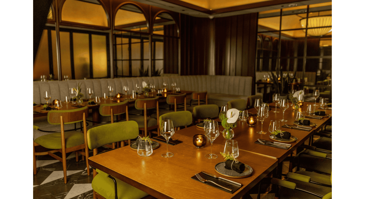 Elegant private dining area with long wooden table, candle lighting, and green velvet chairs in a sophisticated Las Vegas restaurant.