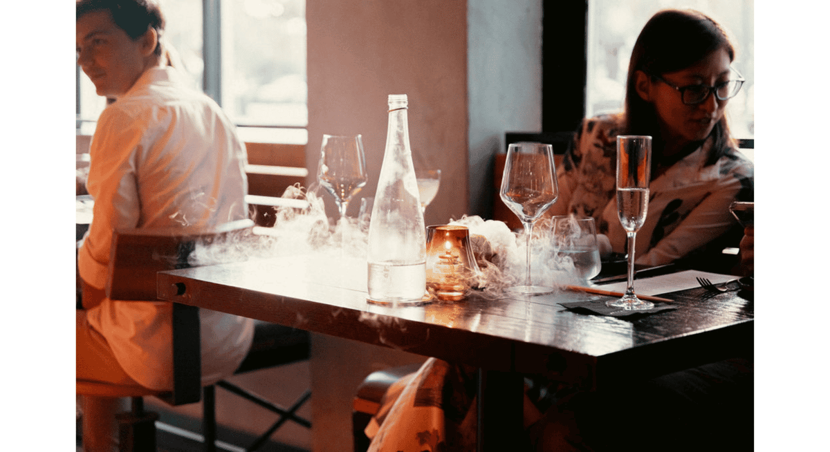 Fine dining table setup with wine glasses, candlelight, and dramatic dry ice presentation in a modern restaurant