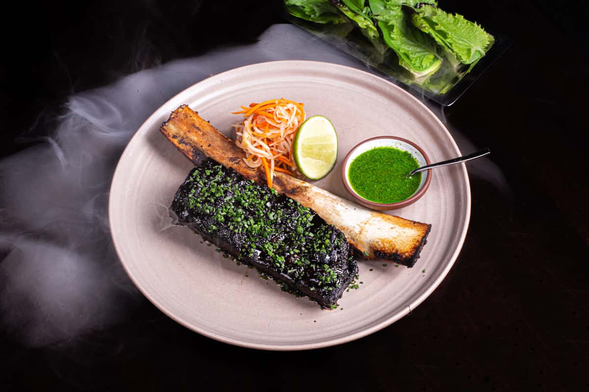 Braised short ribs plated with herbs, lime, and sauce on a dark background