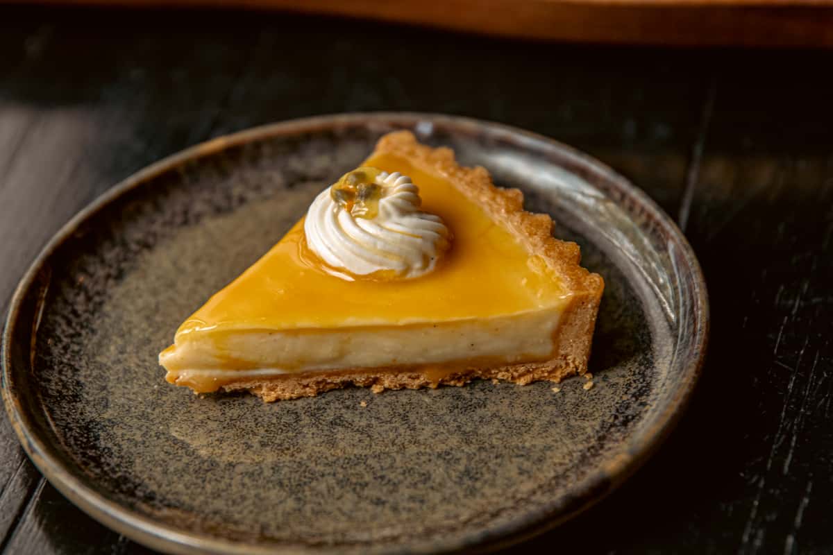 Slice of passion fruit tart topped with whipped cream on a ceramic plate.