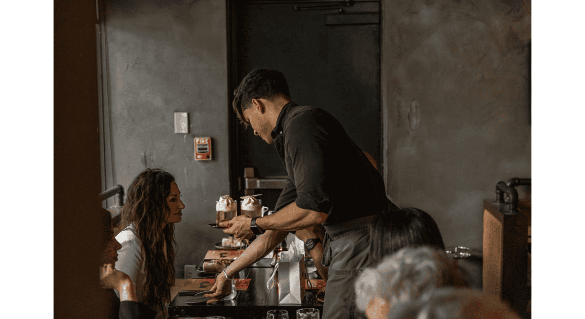 Server presenting crafted drinks to guests inside a modern, softly lit restaurant, showcasing how ambiance and decor enhance memorable dining experiences.