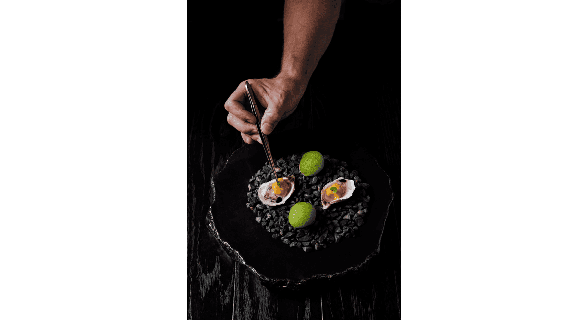 Chef plating gourmet oyster appetizer with tweezers on black stone plate in luxury fine dining restaurant