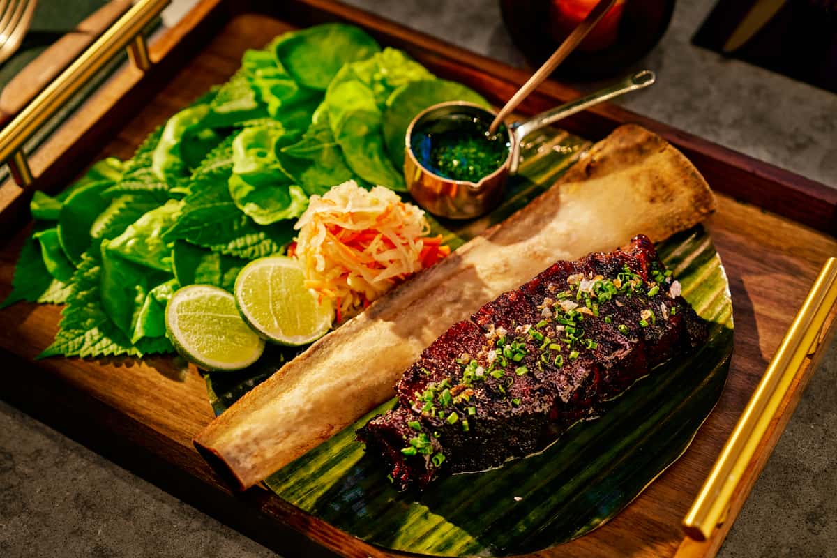 Grilled short rib platter with bone marrow, fresh herbs, lime, pickled vegetables, and dipping sauce.