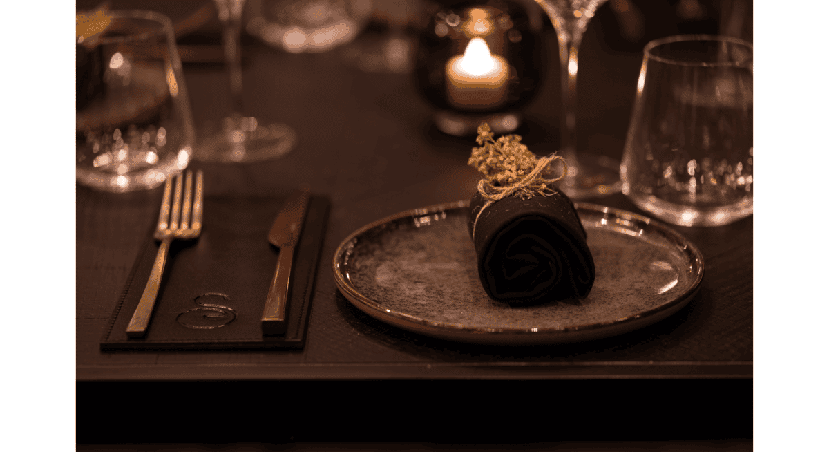 Upscale restaurant table setting with rolled black napkin, candlelight, and fine dining place setting