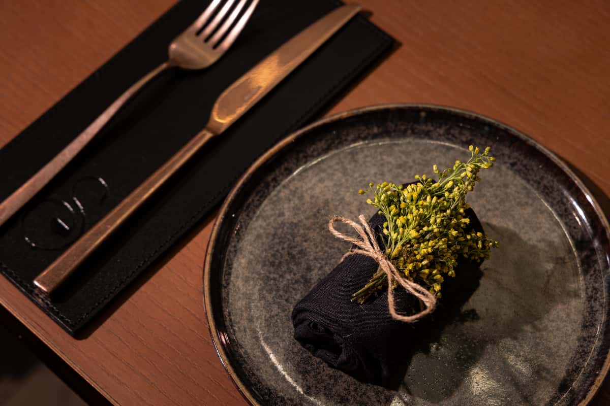 Elegant restaurant table setting with black napkin, decorative flowers, fork, and knife