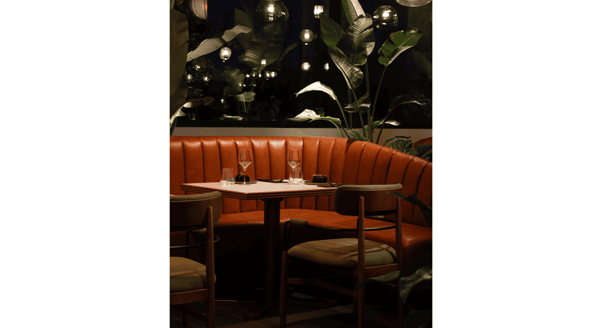 Intimate booth seating with orange leather banquette and candlelit table inside an elegant Las Vegas fine dining restaurant.