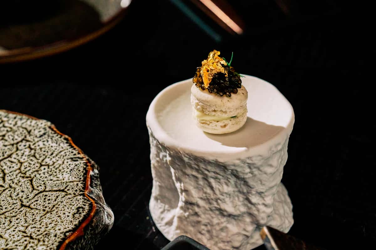 Gourmet macaron topped with caviar, gold leaf, and a delicate herb garnish.