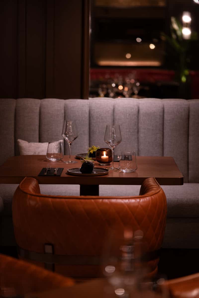 Cozy restaurant table setting with candlelight, wine glasses, and upholstered booth seating