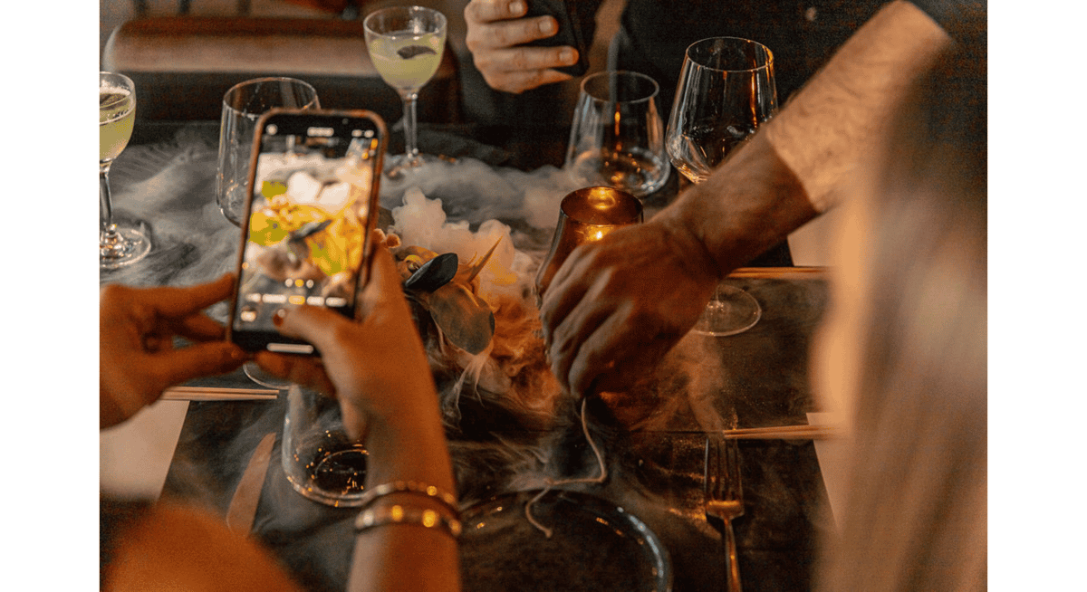 Guests photographing a dramatic plated dish with dry ice smoke during a fine dining restaurant experience
