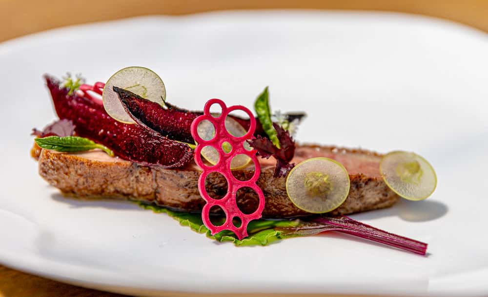 Creative fine dining dish featuring sliced meat, colorful garnishes, and artistic plating on a white ceramic plate.