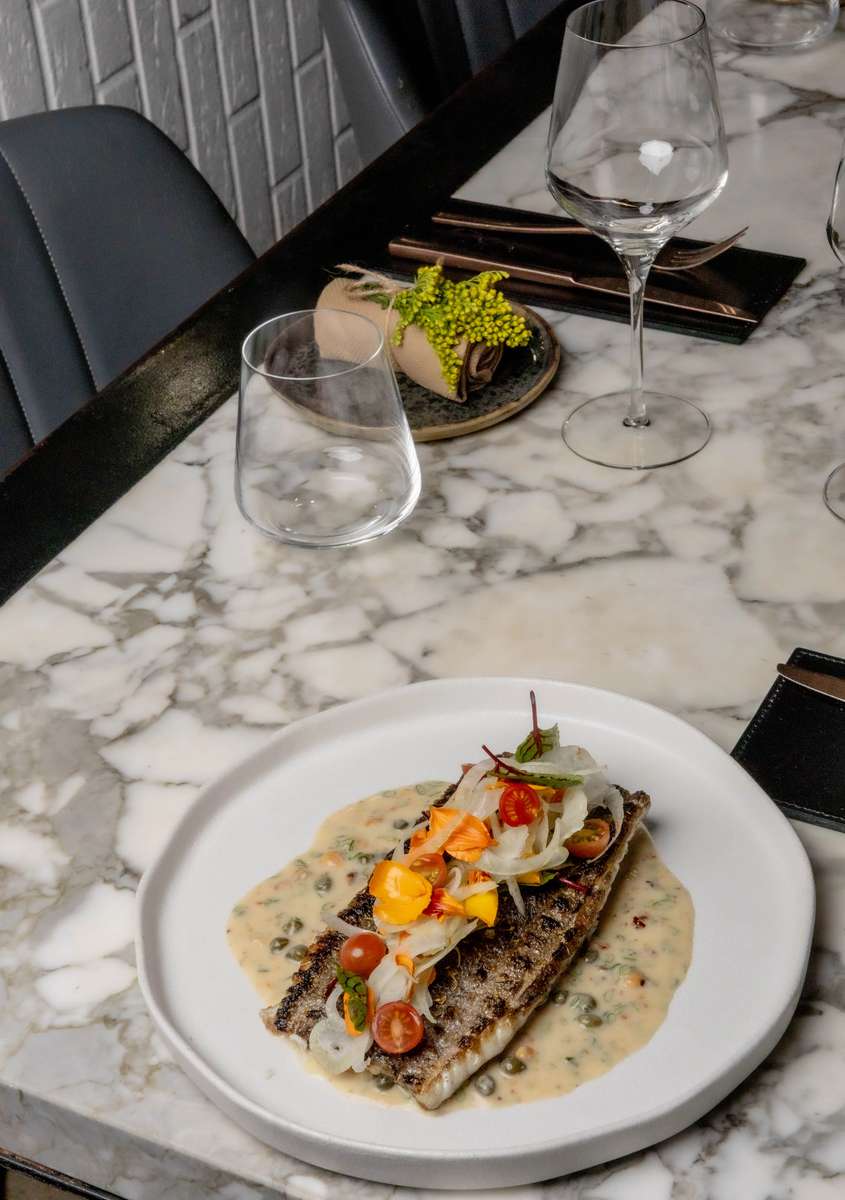 Grilled fish entrée with creamy sauce, fresh garnish, and wine setting at an upscale restaurant table