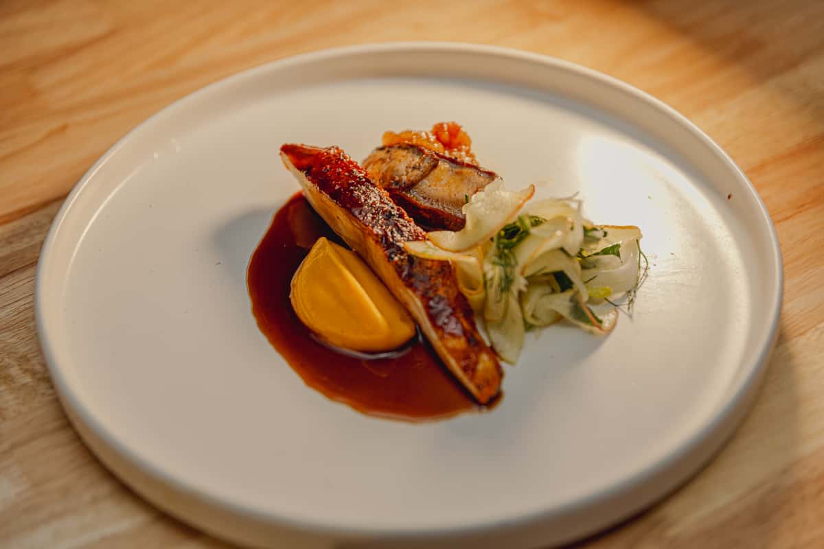 Gourmet seafood dish with seared fish, seasonal vegetables, and sauce plated in an elegant fine dining presentation in Miami.