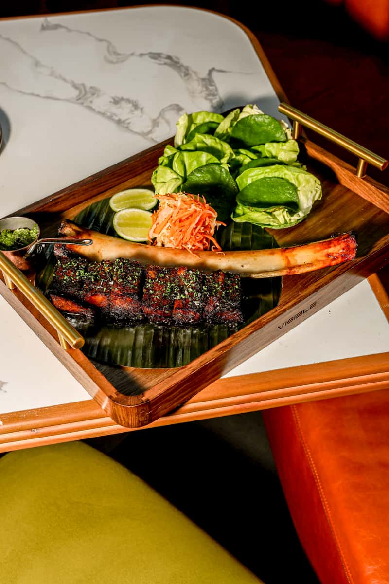 Roasted ribs platter with lettuce wraps, lime, pickled vegetables, and herb sauce.