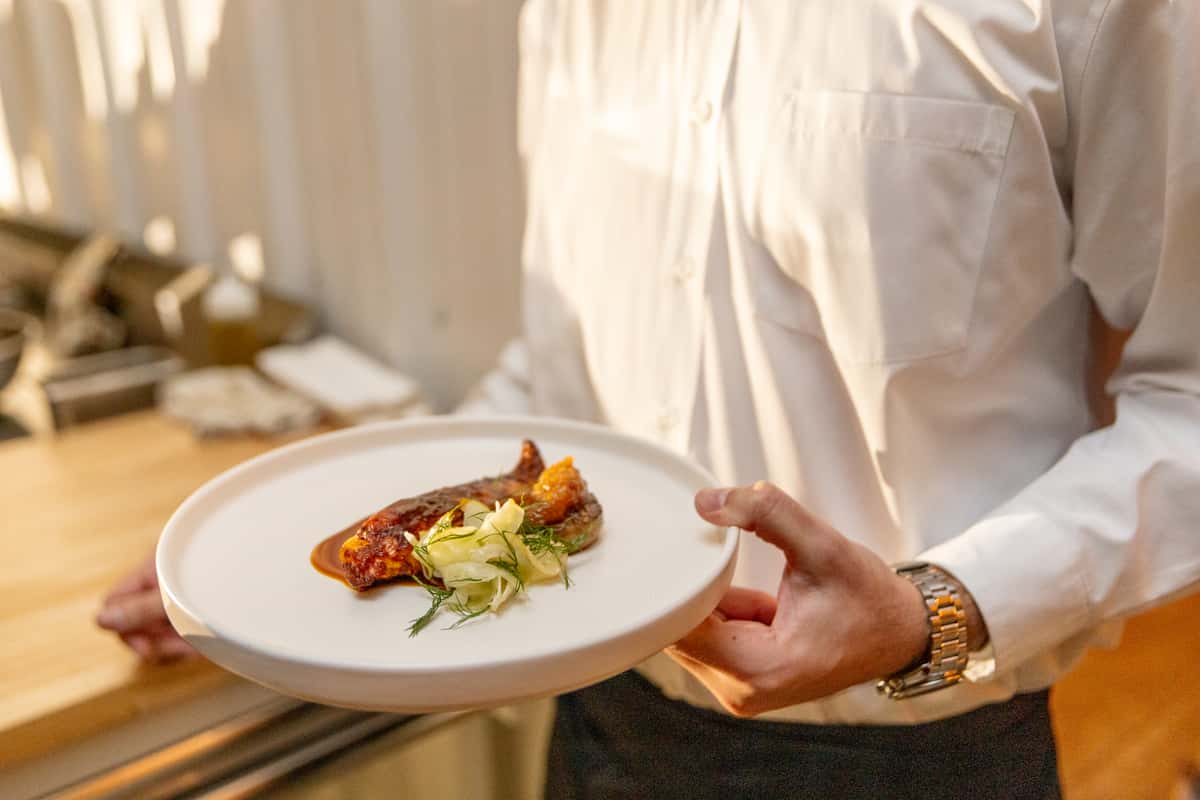 Server presenting a gourmet plated dish during restaurant service