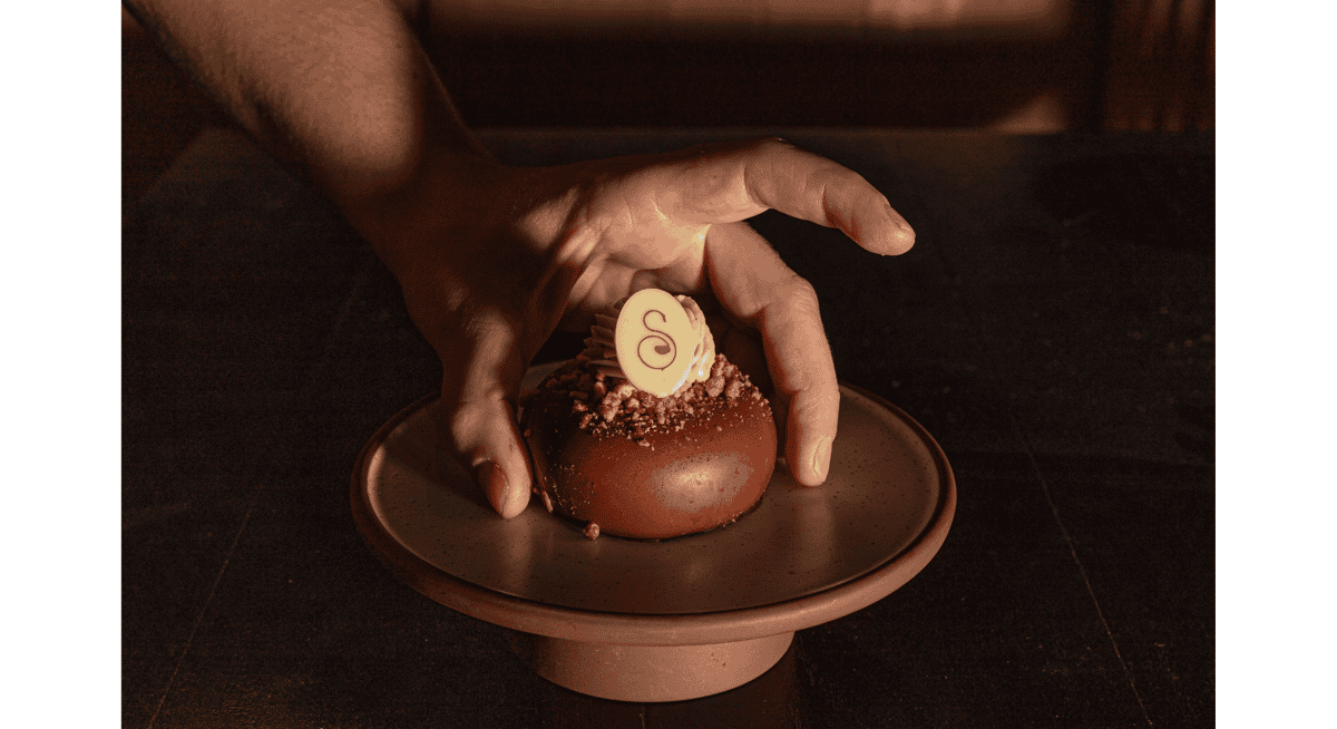 Hand placing a beautifully crafted chocolate dessert on a ceramic plate, illustrating the impact of chef interaction and tableside presentation on guest experience.