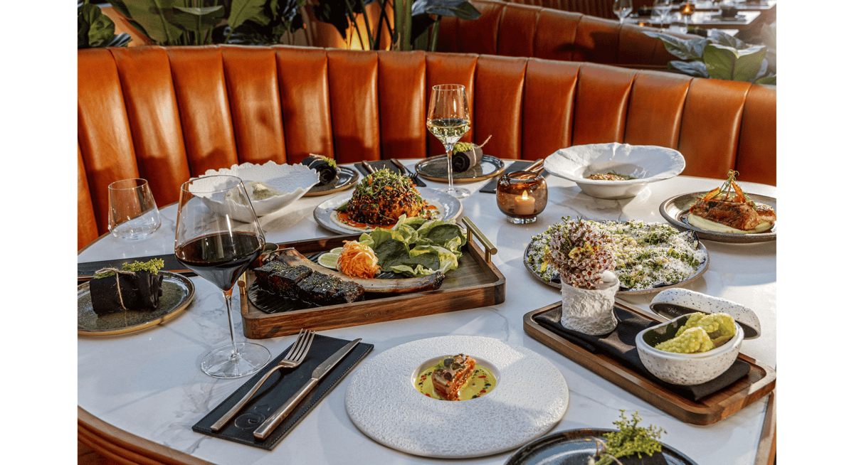 Luxury fine dining table with multiple gourmet dishes, wine glass, and elegant restaurant booth seating