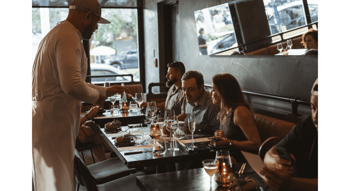 Chef presenting a dish to guests at a candlelit table in an upscale fine dining restaurant.