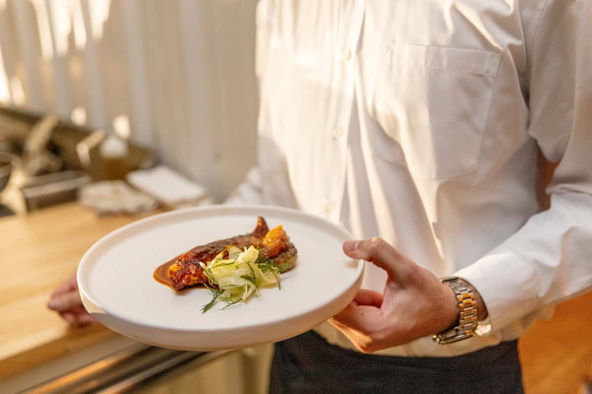 Server presenting an elegant gourmet plated dish in a fine dining restaurant setting