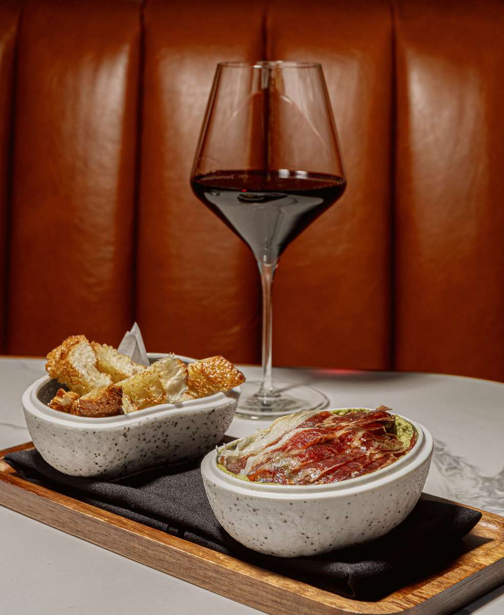 Cured ham tapas served with toasted bread and a glass of red wine.