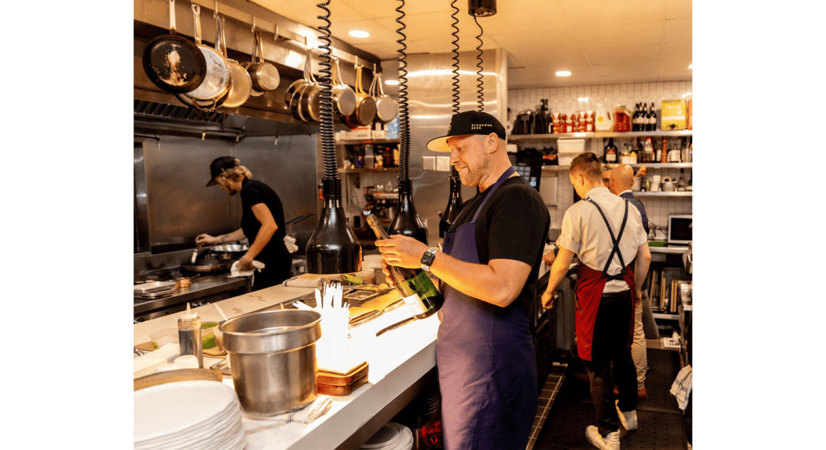 Restaurant kitchen staff preparing dishes and opening wine bottles in a professional fine dining kitchen