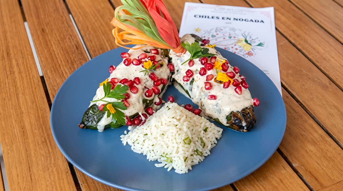Two Chiles en Nogada, covered in white sauce and pomegranate seeds, with white rice on a blue plate.