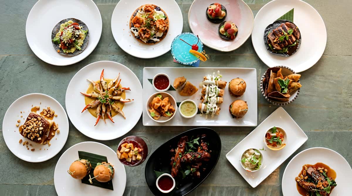 Assortment of appetizers and small plates, including tacos, seafood, pastries, and a blue cocktail.