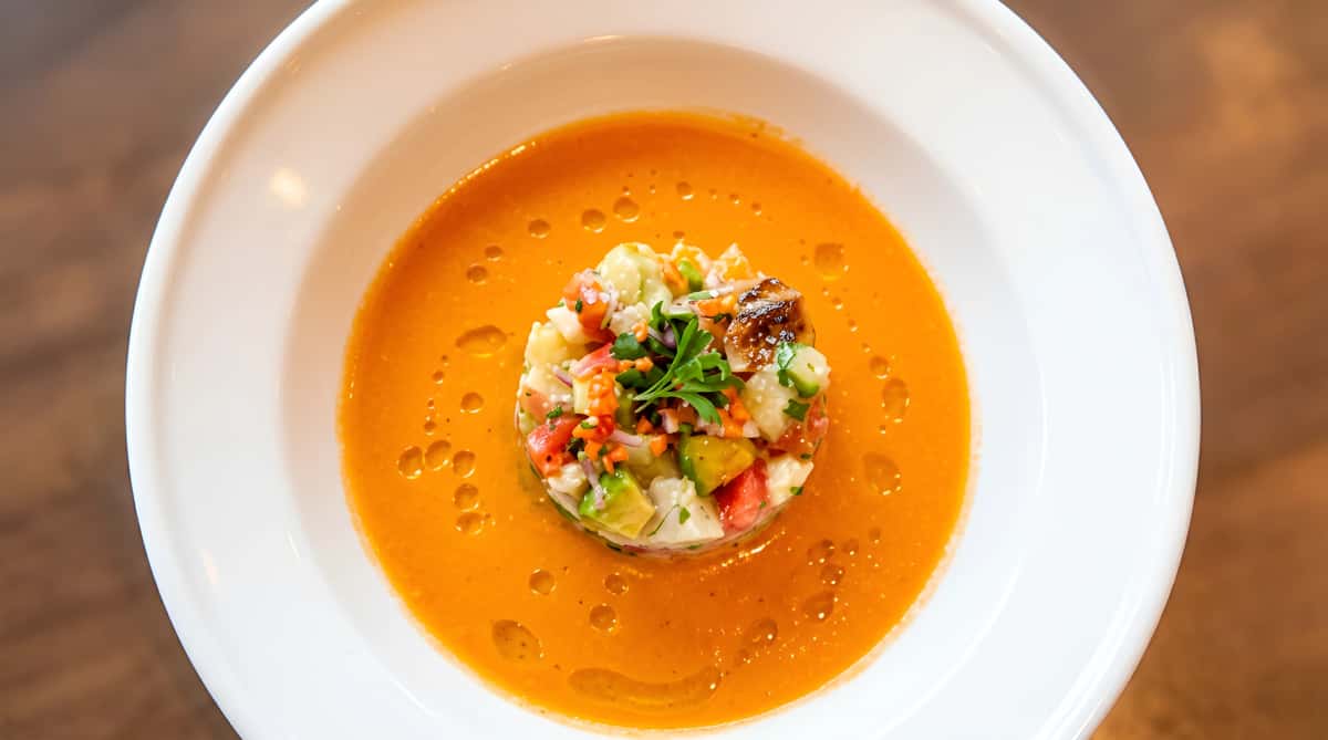 Gazpacho soup with a colorful vegetable medley and herbs in a white bowl.