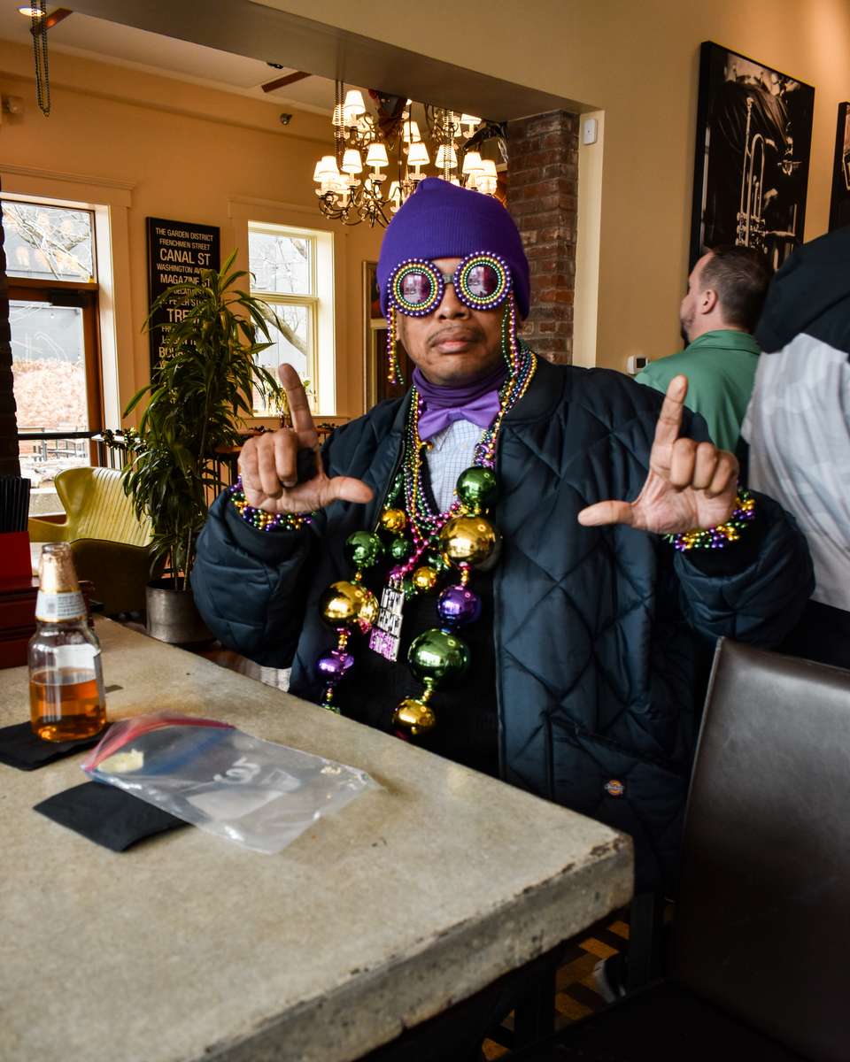 Guest wearing Mardi Gras beads and oversized glasses sits at the bar inside Lou Lou on Market in NuLu, Louisville.