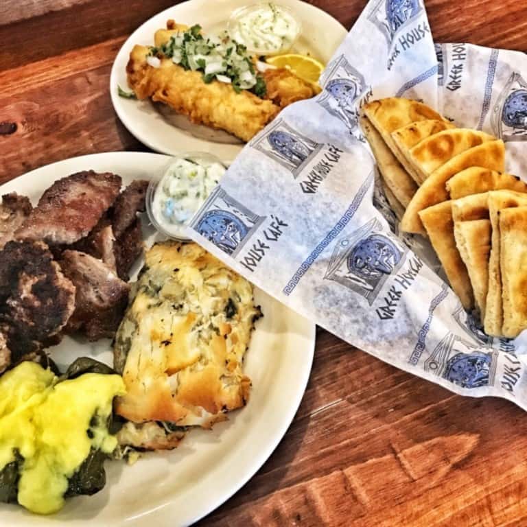 Greek combo platter with gyro meat, spanakopita, dolmas, fried fish, pita bread, and sides of tzatziki and lemon wedges.