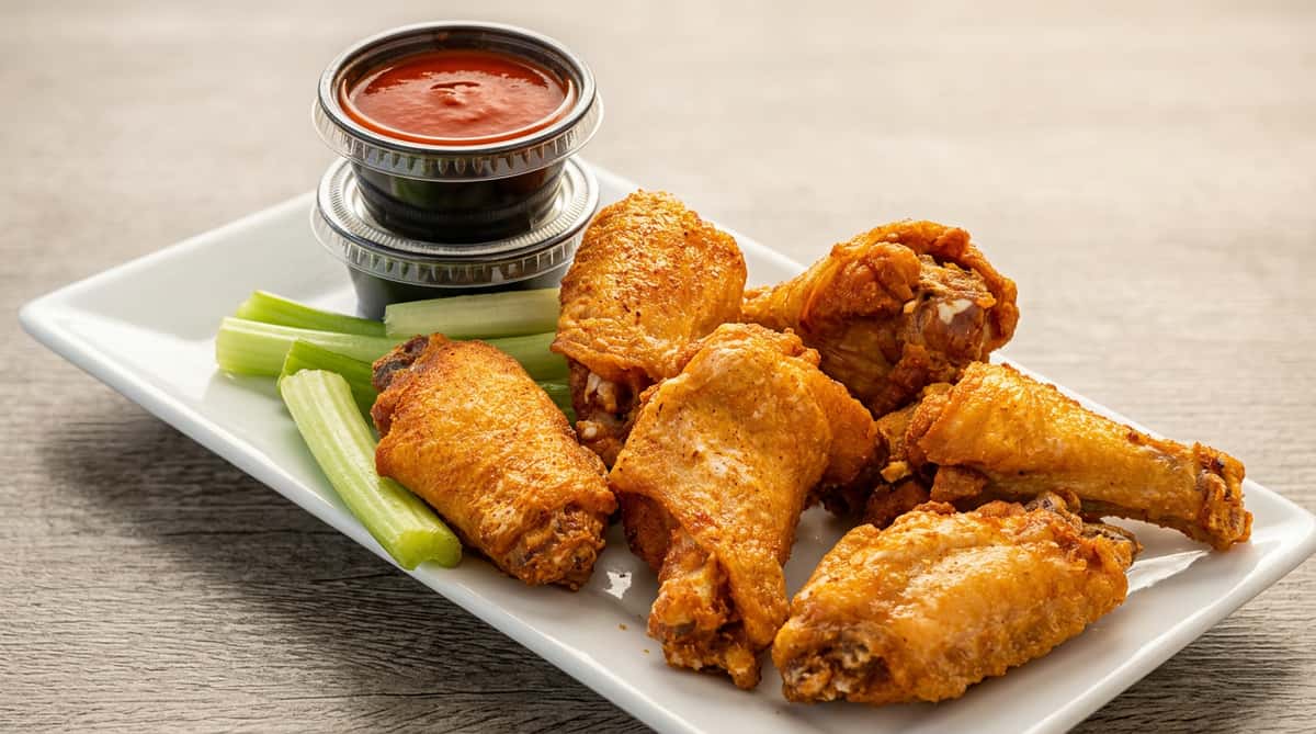 Fried chicken wings with celery sticks and two dipping sauces on a white plate.