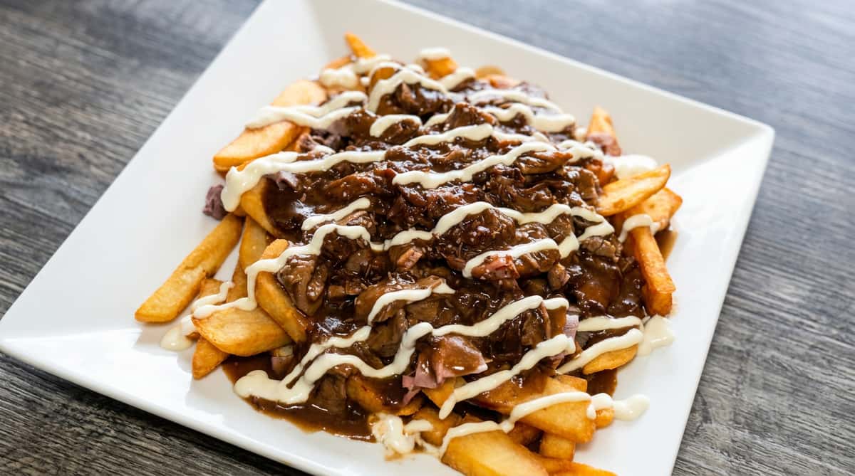 Poutine with french fries, covered in dark gravy, shredded meat, and a drizzle of white sauce.