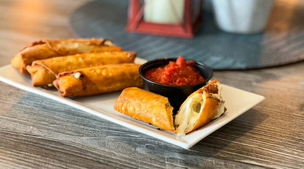 Egg rolls filled with white cheese, one cut open to show melted cheese, served with a side of red marinara sauce.