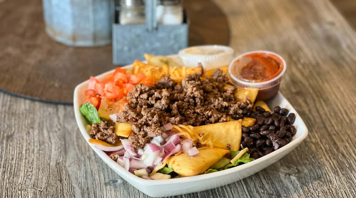 Taco salad with ground beef, tomatoes, red onion, black beans, fried tortilla pieces, and salsa on a white plate.