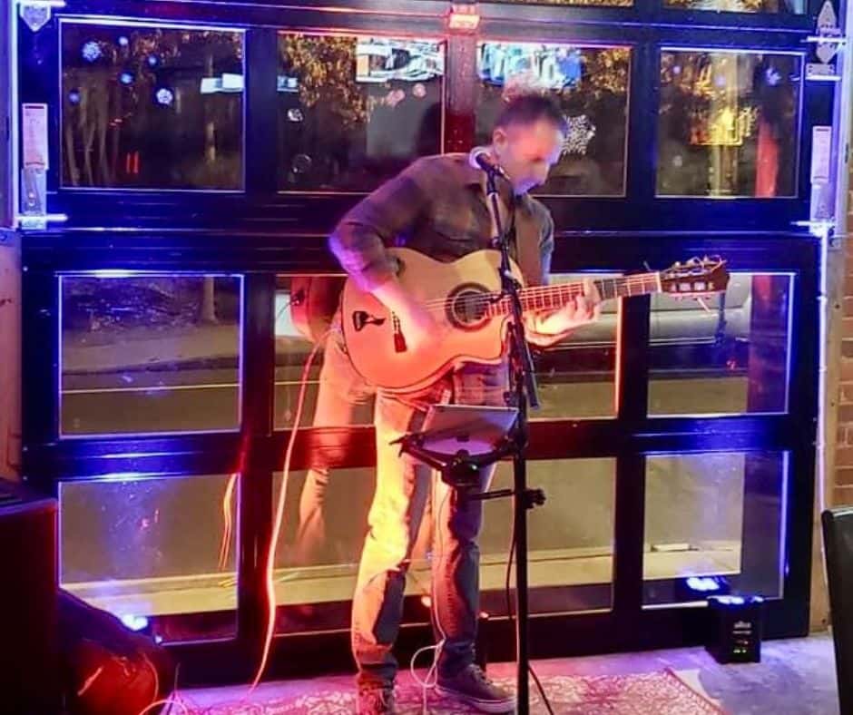 A man sings and plays guitar at night in the bar of Friar Tucks