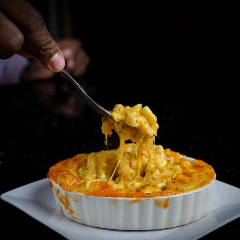 Creamy baked mac and cheese in a white ramekin, with a fork lifting a cheesy bite showing melted cheese stretch.