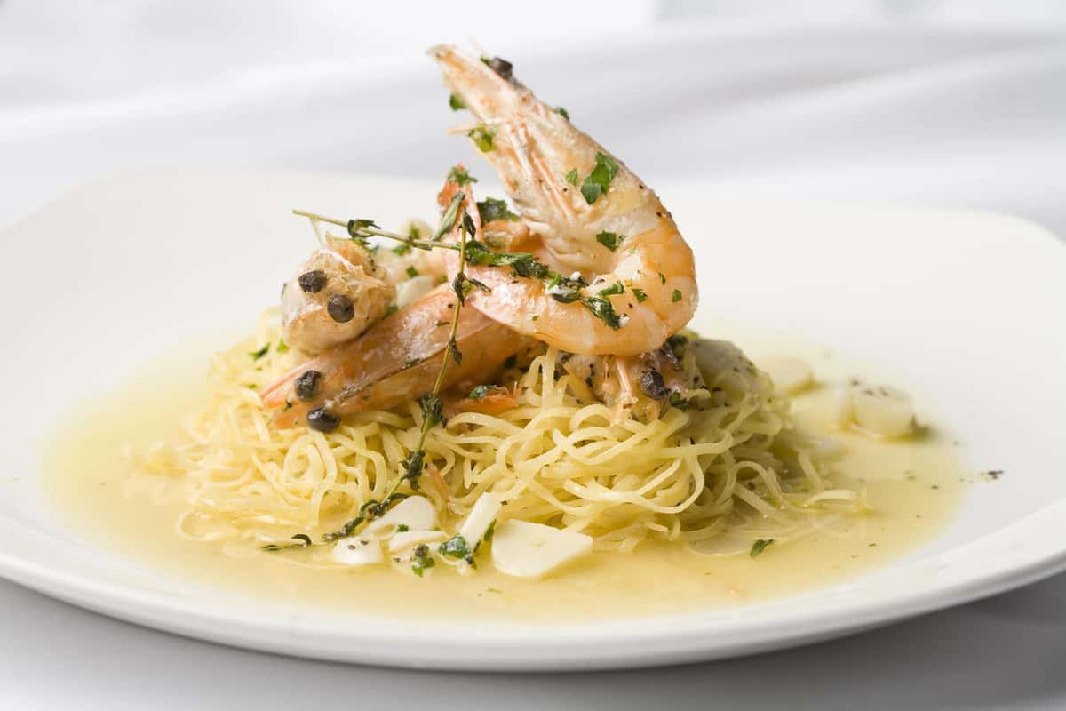 Vinoteca di Monica's elegant shrimp and tagliolini pasta with fresh herbs and a light golden sauce on a white plate.