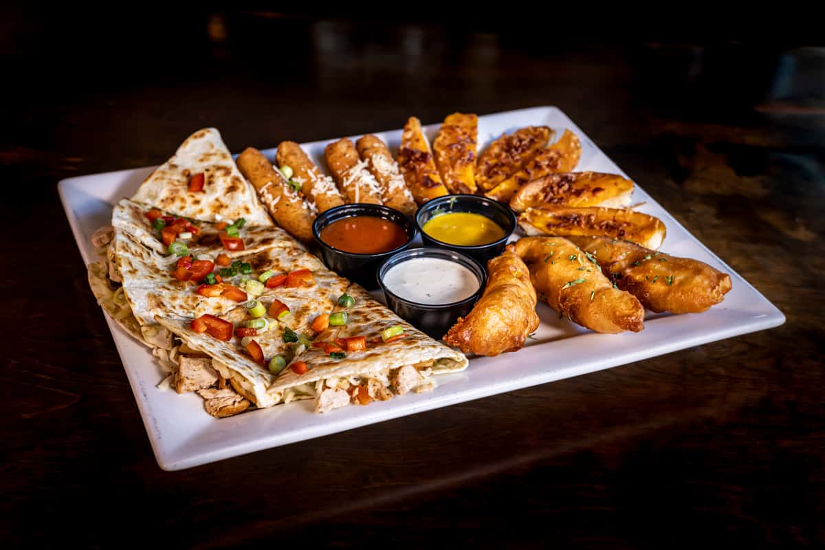 Assorted appetizer platter with quesadilla, mozzarella sticks, potato skins, and fried fish with sauces at Watson's House of Ales.