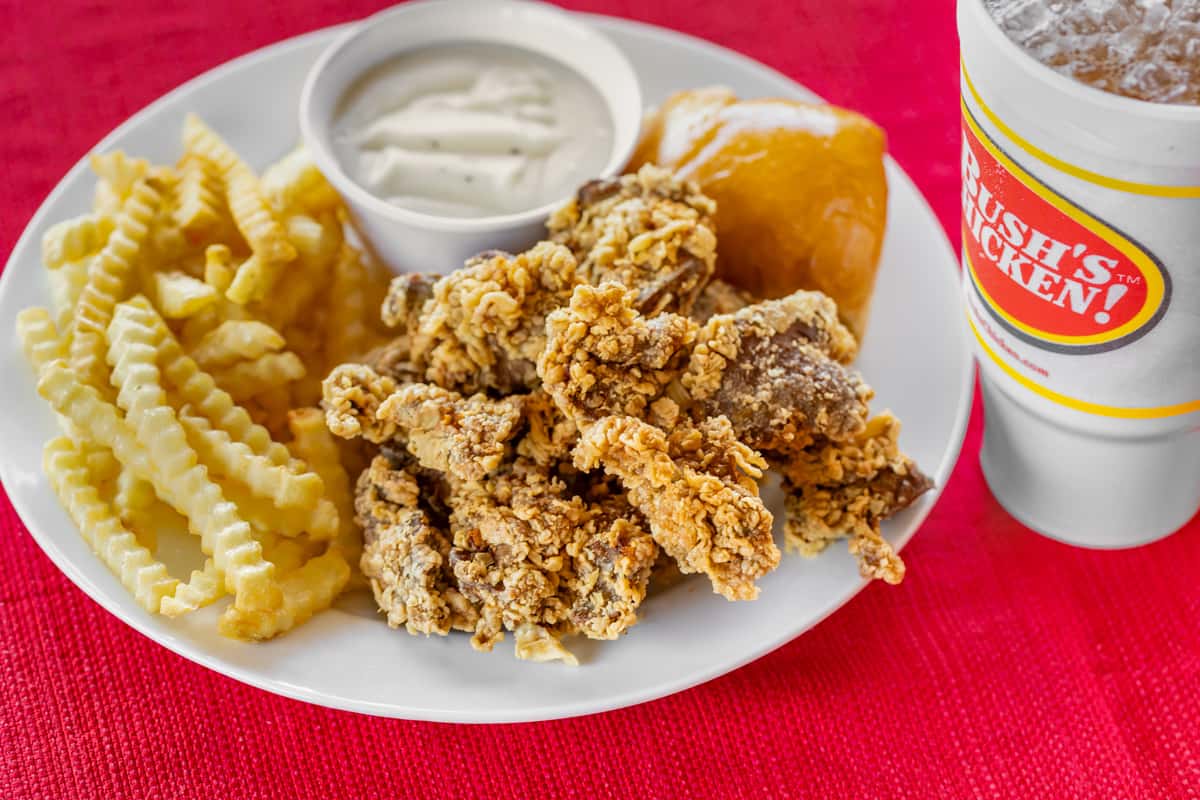 Fried chicken livers meal served with crinkle-cut fries, a warm dinner roll, creamy white gravy, and an iced drink on a white plate over a red tablecloth.