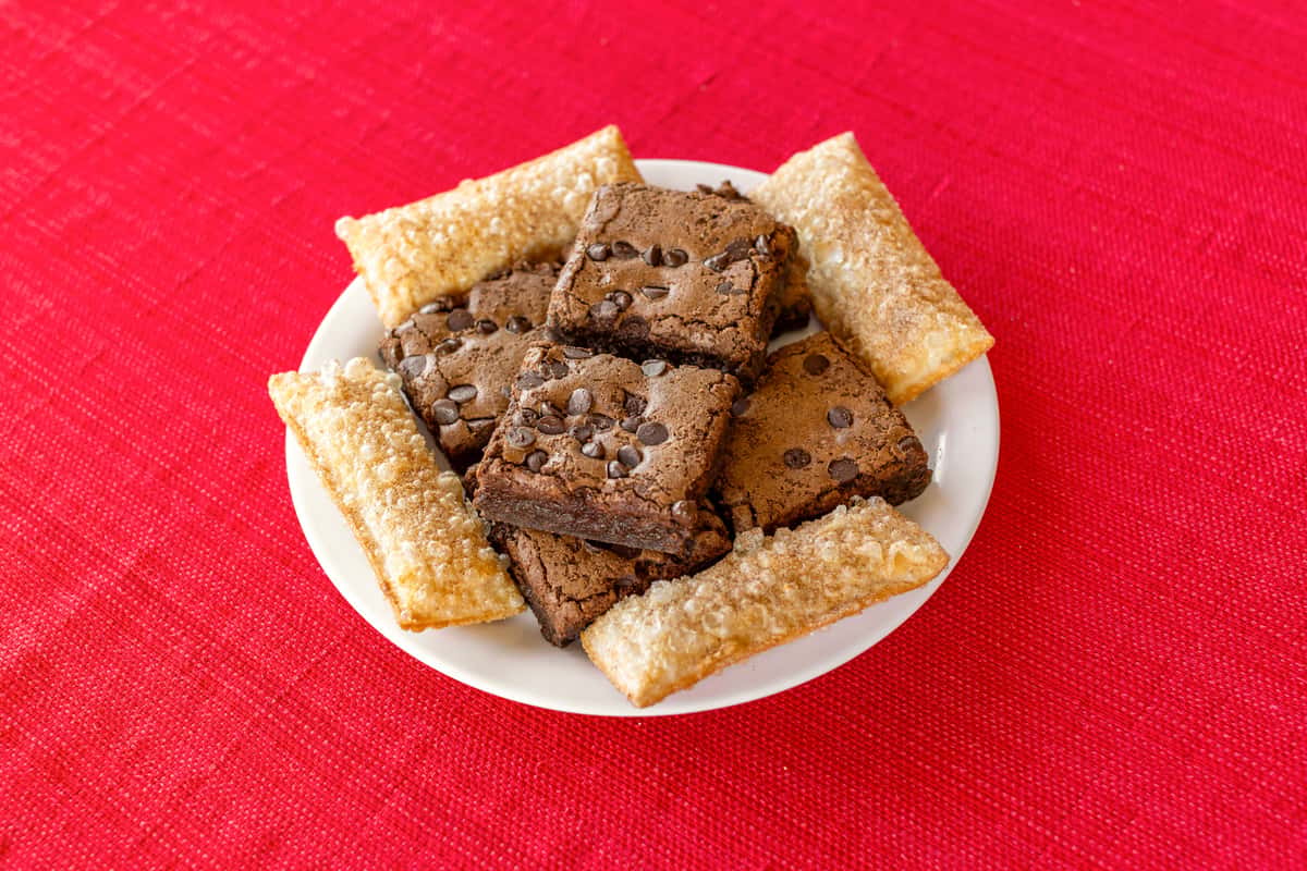 Dessert plate featuring rich chocolate chip brownies and golden, sugar-dusted fried pastries, arranged on a white dish over a bright red tablecloth, ideal for a Southern comfort food finish